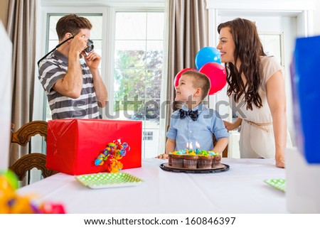 Father taking picture of birthday boy and woman at party
