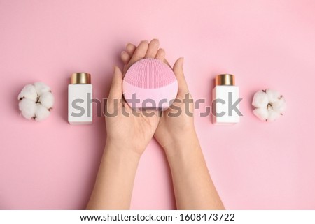 Woman with face cleansing brush on pink background, top view. Cosmetic accessory