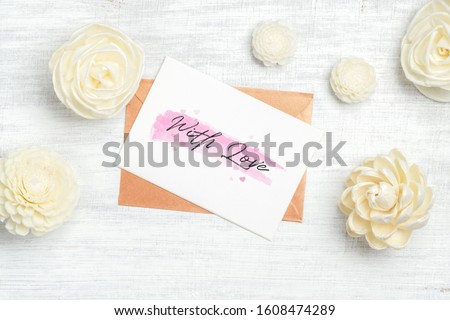 Mockup card and envelop on white wood with with love text and kraft paper roses for Valentine's Day. Mock up for elegant design. Flat lay top view valentine's day background concept.