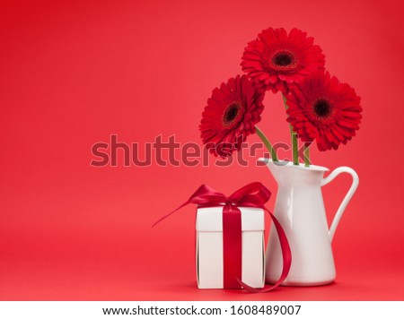 Valentines day greeting card with gerbera flower bouquet and gift box in front of red background with space for your greetings