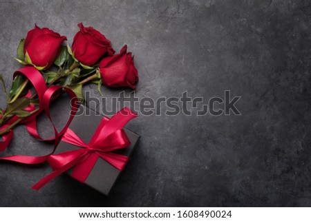 Valentines day greeting card with rose flowers bouquet and gift box over stone background with space for your greetings. Top view flat lay