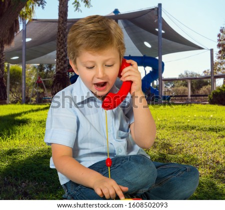 Charming blond boy speaks on a red telephone. Cosy and safe children 's playground with a variety of multicolored attractions. The concept of physical and mental development of children