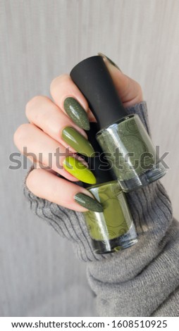 Female hand with long nails and green manicure with bottles of nail polish