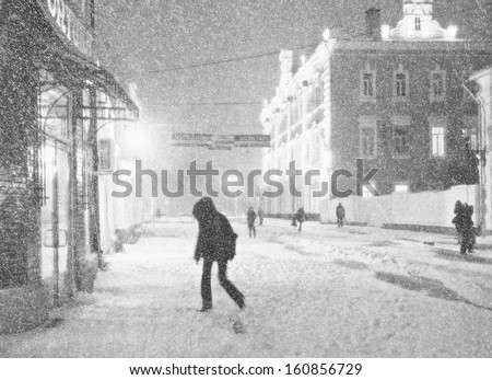 Black-and-white picture of the city street during a snow-storm. Some pedestrians hurry to take cover from a wind.