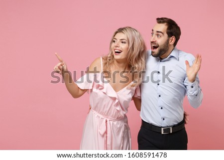 Funny young couple two guy girl in party outfit celebrating posing isolated on pastel pink background. Valentine's Day Women's Day birthday holiday concept. Spreading hands point index finger aside