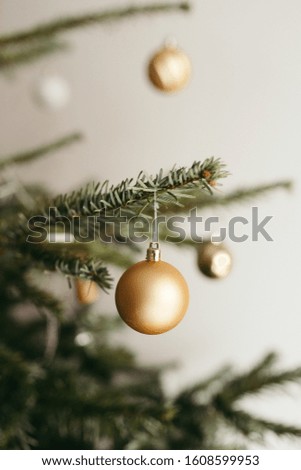 A vertical shot of a Christmas tree decorated with golden baubles against a white wall