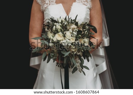 A bride with a white wedding dress holding a beautiful flower bouquet against a black background