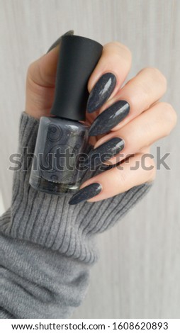 Female hand with long nails gray manicure and a bottle of nail polish