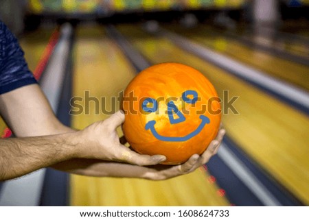 hands holding a bowling ball on the background of bowling lanes. A smiley is drawn on the ball.