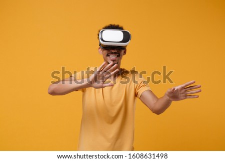 Funny young african american guy in casual t-shirt posing isolated on yellow orange background in studio. People lifestyle concept. Mock up copy space. Watching in headset waving hands, showing palms