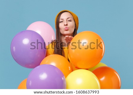 Young woman girl in sweater hat posing isolated on blue background. Birthday holiday party, people emotion concept. Mock up copy space. Celebrating hold colorful air balloons blowing sending air kiss