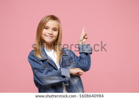 Smiling little kid girl 12-13 years old in denim jacket isolated on pastel pink background children studio portrait. Childhood lifestyle concept. Mock up copy space. Pointing index finger aside up Royalty-Free Stock Photo #1608640984