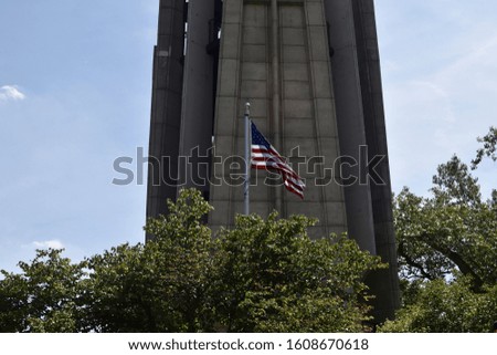 A tall tower surrounded by greenery with the American flag in front of it under sunlight in Illinois