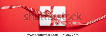 Banner of white gift box with a red ribbon bow on red background. Flat lay top view. Presents and holidays concept