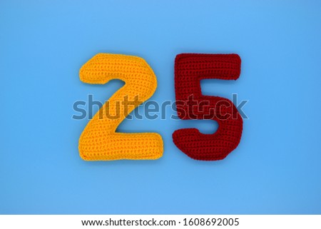 The number 25 is tied from yellow and red yarn on a blue background. Design, creative, handmade, decor, amigurumi.