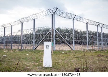 Border fence between Subotica (Serbia) & Kelebia (Hungary) with a boundary marker. This border wall was built in 2015 to stop the incoming refugees & migrants during the refugees crisis Royalty-Free Stock Photo #1608724438