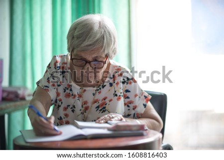 old woman Sitting and writing on the table by the glass window in the house To train the brain and memory Not to be forgotten. Stay at home and Prevent dementia. Royalty-Free Stock Photo #1608816403
