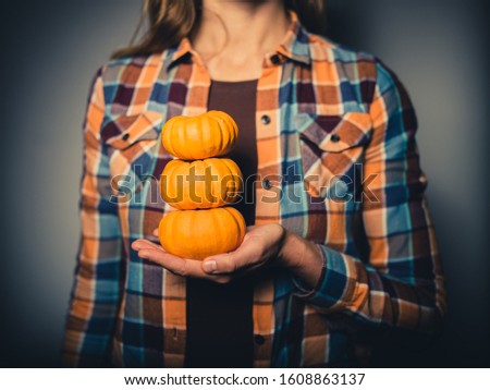 Studio shot of young woman holding a stack of small pumpkins