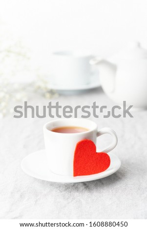 Valentine's Day. Morning breakfast for two with tea and flowers. Red felt heart is symbol of lovers. Light white tender pastel background. Vertical, copy space. Scandinavian minimalism