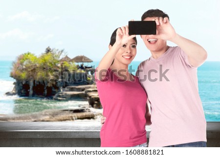 Asian couples making a selfie using a camera phone with Tanah Lot Temple background