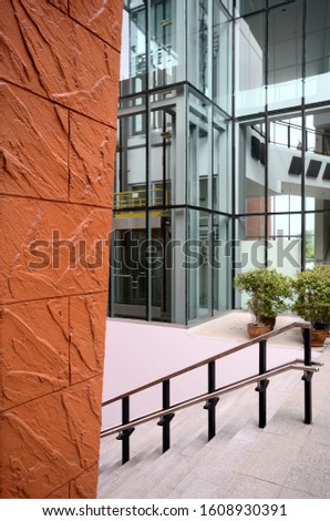 Vertical view of brown wall and steps opposite modern glass wall building and transparent elevator ,good for advertisement
