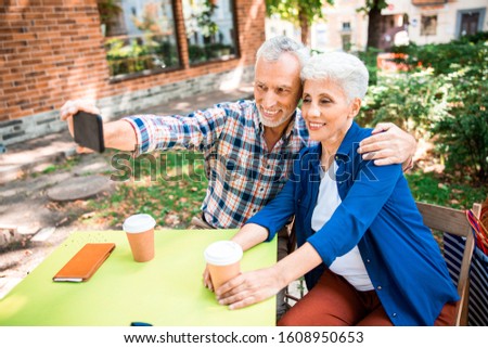 Smiling elderly gentleman hugging wife and taking picture with smartphone stock photo