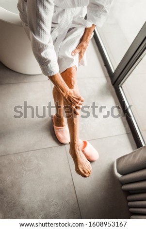 Close up of old female hand applying foot cream stock photo