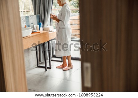 Old lady looking at drink and smiling while spending time in spa salon stock photo. Website banner