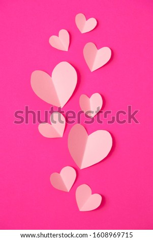Paper elements in shape of heart flying on pink paper background. Love and Valentine's day concept. Birthday greeting card design.