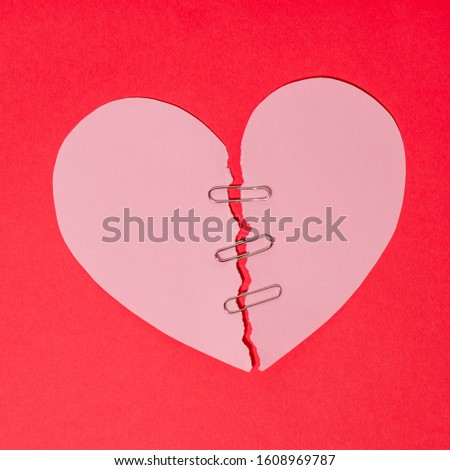 Red paper heart torn in half secured with safety clip on red background