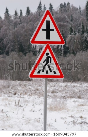 
icy road sign of a crosswalk and a dangerous intersection against a snowy forest in winter