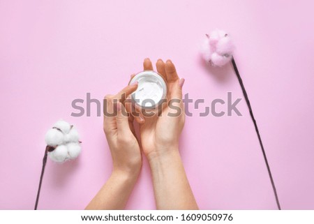 Hands of young woman and jar of cream with cotton flowers on color background