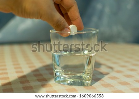 Tablet of sedative in a hand above a glass with water