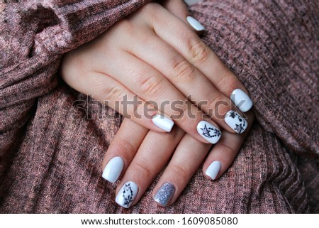 Two female hands with white manicure with black and silver stars on beige background. Stylish fashionable woman's manicure. Nail polish. Artistic manicure. Modern style. Winter manicure.