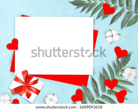 Mock up empty paper blank with red hearts, cotton flowers, gift, palm leaves on blue textured background. Valentines day, Mothers day or wedding invitation concept. Flat lay