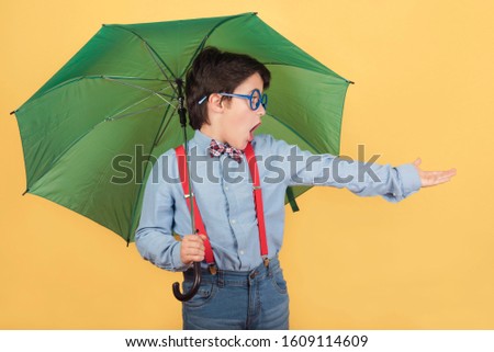 child with green umbrella on yellow background