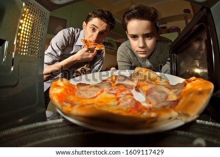 The guys get pizza from the microwave. Food heating in the home kitchen. Fast food.  Cooking at home. Men eating pizza.