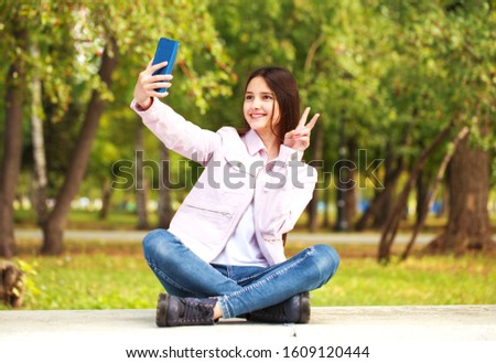 Young beautiful girl photographs herself on a cell phone while sitting in an autumn park.
