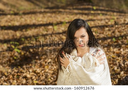 cold woman wraps blanket over herself while standing in color autumn park