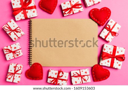 Top view of craft notebook surrounded with hearts and gift boxes on colorful background. Valentine's day.
