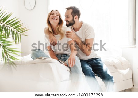 Happy young couple in love relaxing on a couch at the living room, rading magazine, embracing