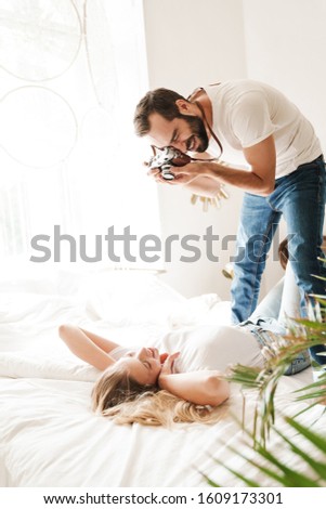 Cheerful young couple taking photos indoors while laying on bed at home