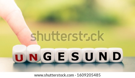 Hand turns dice and changes the German word "ungesund" ("unhealthy" in English) to "gesund" (" healthy" in English).