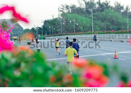Unidentified professional and amateur athletes are participating in a jogging/ marathon event. Photo taken from behind with prominent Bougainvillea flowers