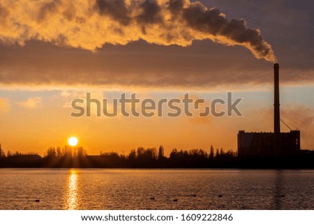 Power plant smokestack at sunrise near the lake. Environmental pollution.