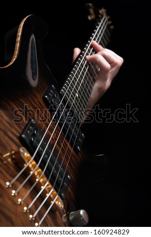 close up shot of male hand playing vintage brown guitar over black - shallow DOF with focus placed on strings