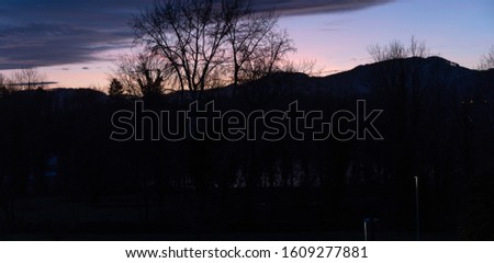 Dramatic sunset with pink blue clouds over bar trees and hills in wintertime without snow. Pictures unprocessed and original. In Switzerland.