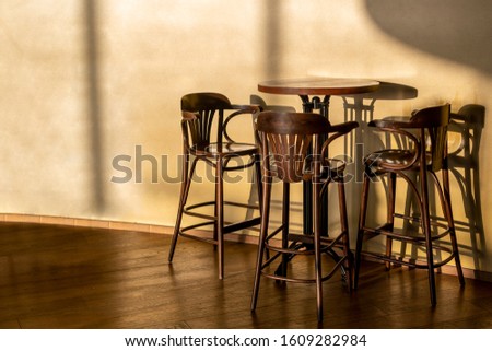 Tall vintage wooden table and chairs stand in a cafe. A light, cool shadow from sunlight reflects on the wall and floor. A clear shadow from the furniture. Horizontal close-up