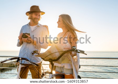attractive happy couple traveling in summer on bicycles, man and woman with blond hair boho hipster style fashion having fun together, looking in map sightseeing taking photos on camera