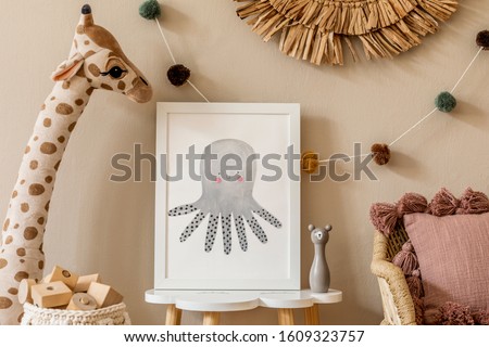 Stylish and modern scandinavian newborn baby interior with mock up photo frame on the small table. Toys, sofa, plush animal and hanging cotton colorful balls. Beige wall. Design home staging. Template Royalty-Free Stock Photo #1609323757